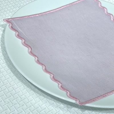 Guardanapo de tecido rosa claro com borda ondulada sobre prato branco