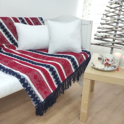 Manta colorida de lã sobre sofá branco com almofadas, mesa com chávenas e decoração natalícia