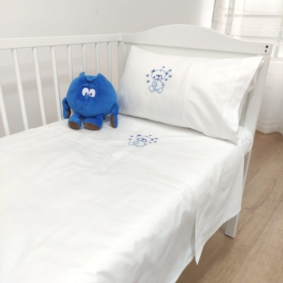 Cama de bebé com lençóis brancos e bordados azuis de ursinho e peluche azul