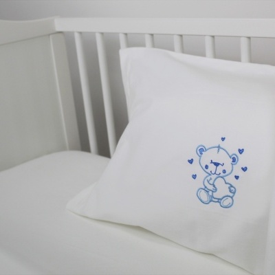 Almofada branca com bordado azul de urso num berço branco.