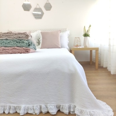 Cama com colcha branca, cobertores pastel, almofadas e decoração minimalista