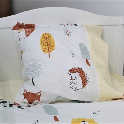 Berço branco com roupa de cama infantil colorida e decorada com animais e árvores