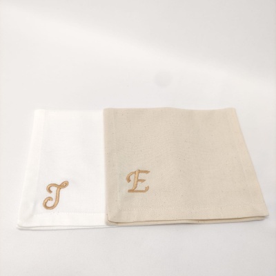Dois panos de prato bordados, um branco com letra J dourada e outro bege com letra E dourada