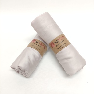 Dois rolos de tecido branco com etiquetas AGTEX de papel castanho sobre superfície branca