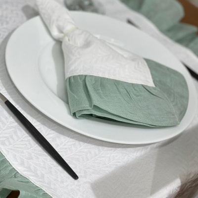 Guardanapo de tecido verde claro e branco sobre prato branco em mesa posta