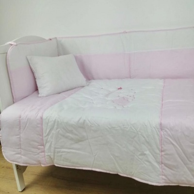 Cama de bebé com colcha acolchoada rosa e branca e almofada pequena branca