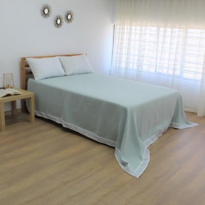 Cama de casal com colcha verde água, duas almofadas brancas e decoração simples no quarto