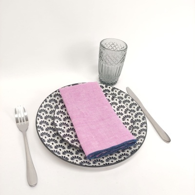 Conjunto de loiça com prato decorado preto e branco, guardanapo rosa, talheres metálicos e copo transparente