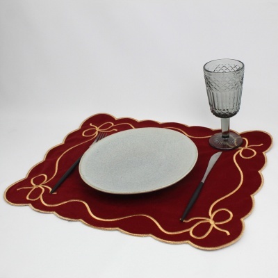 Conjunto de jantar com prato branco, talheres com cabo preto e copo de vidro sobre toalhete vermelho bordado