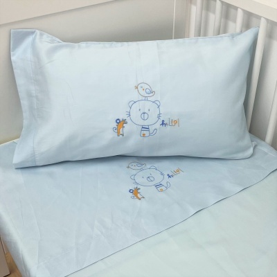 Jogo de cama azul claro com bordado de ursinho, pássaro e esquilo num berço branco