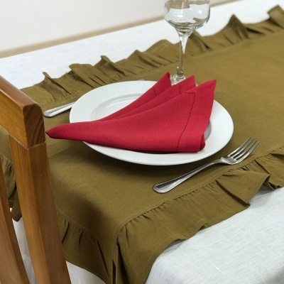 Mesa posta com toalha branca, cobertura verde com babados, guardanapo vermelho, prato branco, talheres e copo de vidro