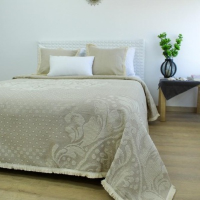 Cama com colcha bege e almofadas, mesa de madeira com vaso e plantas, ambiente claro e minimalista