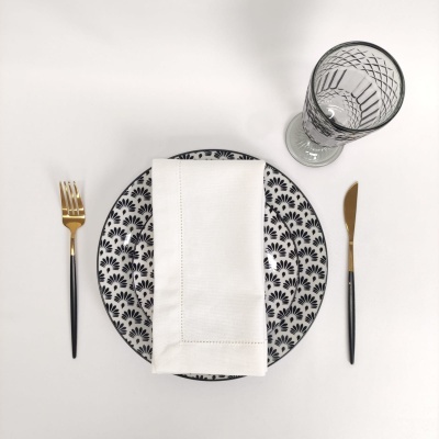 Conjunto de mesa com prato estampado, guardanapo branco, talheres pretos e dourados e copo de vidro