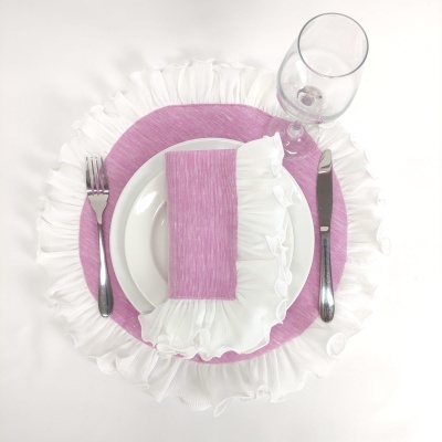 Conjunto de mesa com guardanapo rosa e branco, prato branco, sousplat rosa com volantes, talheres e taça.