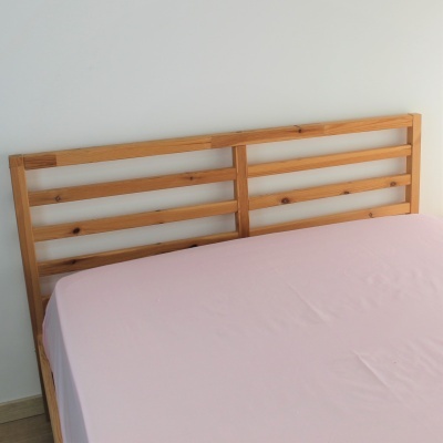 Cabeceira de cama em madeira com barras horizontais e colchão com lençol rosa