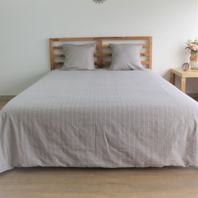 Cama com lençóis cinza riscado e cabeceira de madeira clara