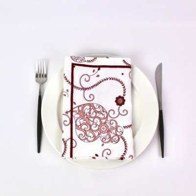 Guarda-napo branco com padrão vermelho e castanho sobre prato branco com talheres