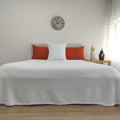 Cama com colcha branca e almofadas laranja e branca numa sala minimalista