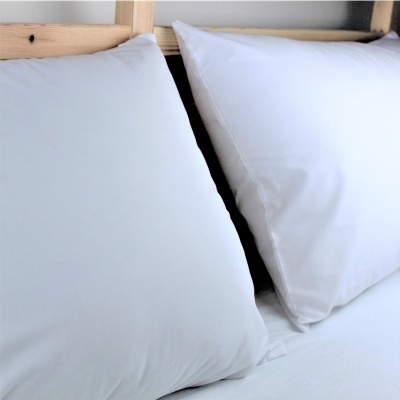 Dois pilares brancos com fronhas brancas em cama com cabeceira de madeira.