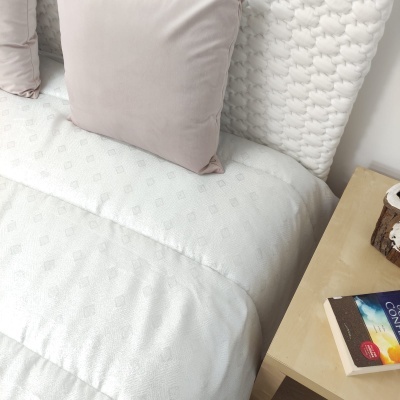 Cama com roupa branca e almofadas creme junto a mesa de cabeceira com livro