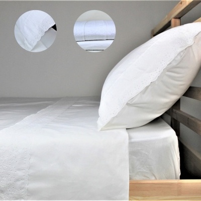 Conjunto de roupa de cama branco com bordados florais e estrutura de cama em madeira clara.