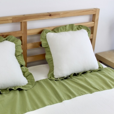 Almofadas e colcha em branco e verde numa cama de madeira clara