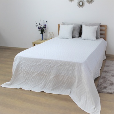 Cama com colcha branca e almofadas ao lado de mesa de cabeceira com vaso de flores