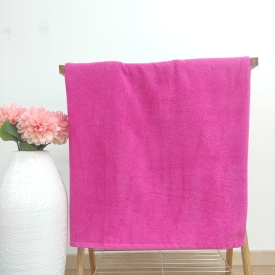 Toalha cor de rosa pendurada num cabide de madeira ao lado de vaso branco com flores
