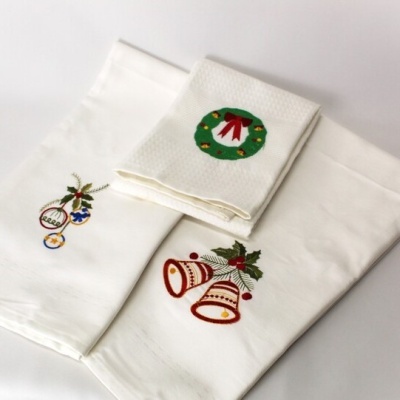 Três toalhas brancas com bordados natalícios coloridos sobre superfície clara