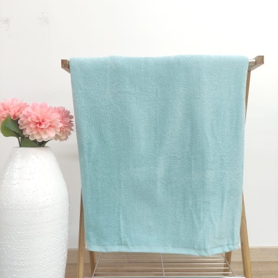 Toalha azul clara pendurada em suporte de madeira ao lado de vaso branco com flores cor-de-rosa