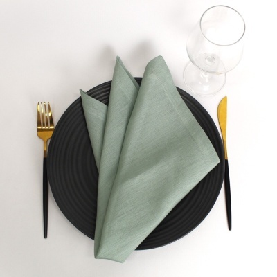 Conjunto de mesa com prato preto, guardanapo verde, talheres preto e dourado e copo transparente.