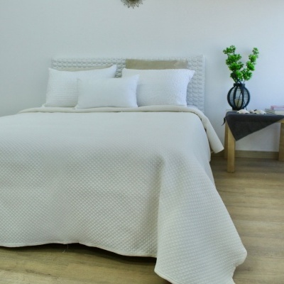 Cama casal com colcha e almofadas brancas, mesa com vaso de flores verdes