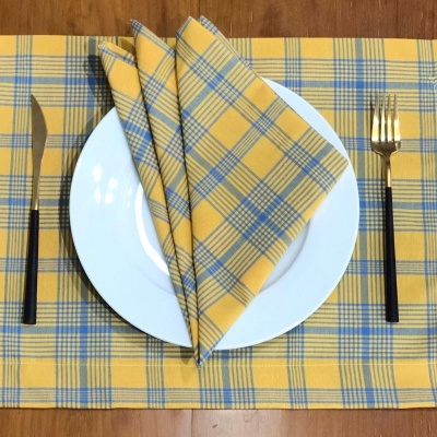 Jogo americano amarelo com xadrez azul, prato branco e talheres com cabo preto