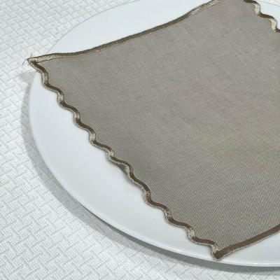 Guardanapo castanho claro com borda ondulada castanha sobre prato branco em superfície texturizada branca