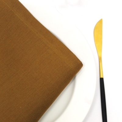 Guardanapo castanho sobre prato branco com faca dourada e preta ao lado
