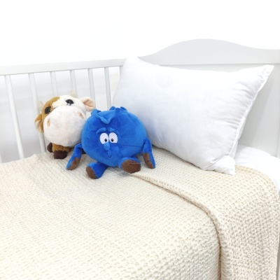 Cama branca de criança com roupa de cama bege e almofada branca e dois peluches.