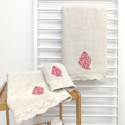 Conjunto de toalhas bege com bordado vermelho e renda, arrumadas em suporte de madeira e toalheiro branco