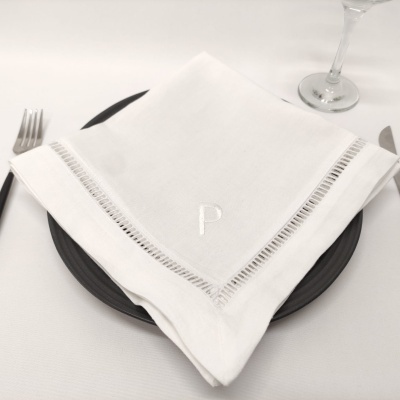 Guardanapo branco bordado com letra P em prato preto numa mesa posta