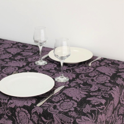 Toalha de mesa preta com padrão floral roxo, pratos brancos, copos de vidro e talheres prateados sobre mesa.