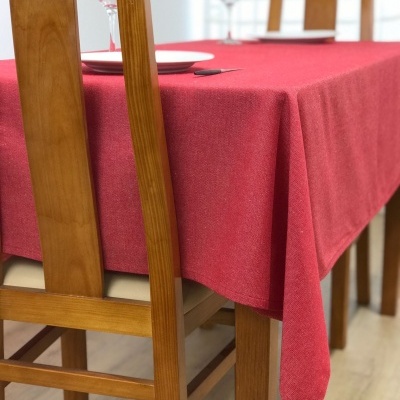 Mesa de madeira com toalha vermelha, cadeiras, pratos e copos em ambiente interior.