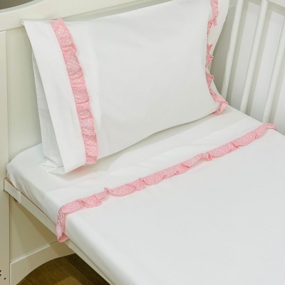 Roupa de cama branca com friso rosa para berço numa cama branca de madeira.