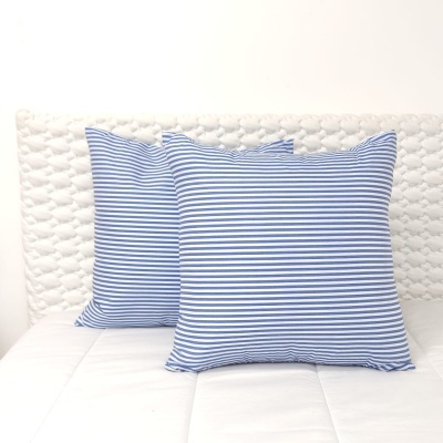 Duas almofadas riscas azul e branco sobre cama branca com cabeceira acolchoada branca