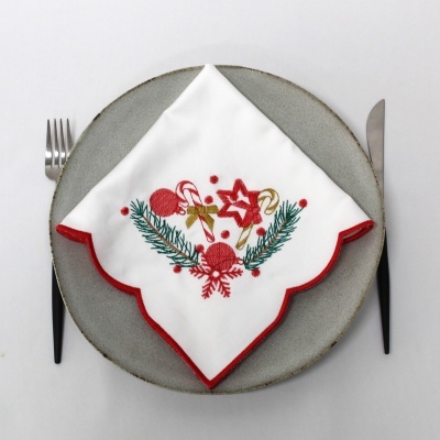 Guardanapo natalício bordado branco com borda vermelha em prato cinza com talheres.
