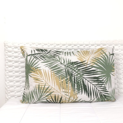 Travesseiro decorativo com padrão de folhas tropicais verdes e douradas numa cama branca