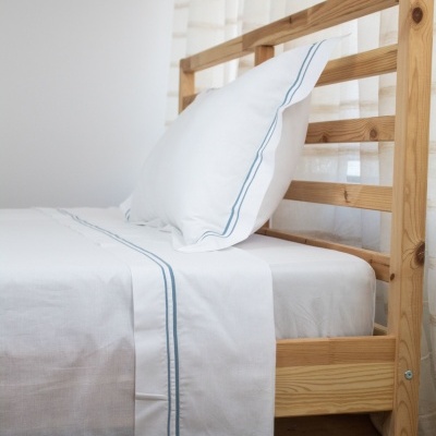 Cama de madeira com lençol branco com linhas azuis e almofada