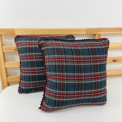 Duas almofadas xadrez azul escuro, vermelho e branco com borda vermelha sobre colchão branco e cabeceira de madeira.