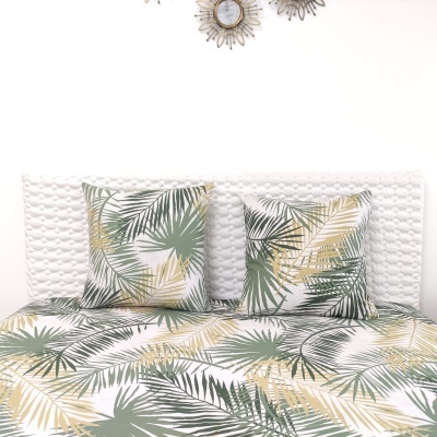 Jogo de cama com padrão de folhas tropicais em verde e bege, duas almofadas, cama branca com cabeceira texturizada e decoração na parede.