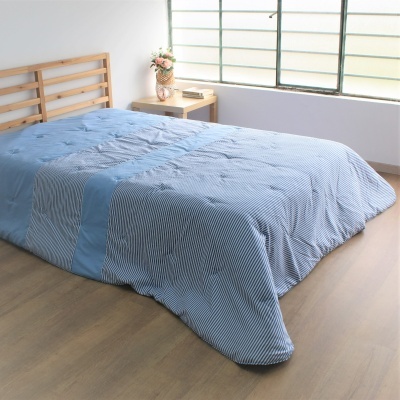 Cama com colcha azul riscada e estrutura de madeira clara junto a janela grande