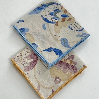 Dois panos de cozinha estampados dobrados, um com padrão azul e bege, outro com padrão roxo e amarelo.