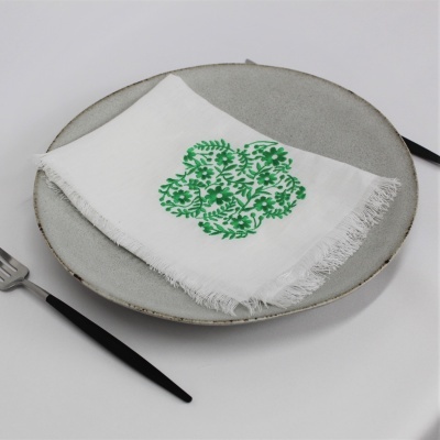 Guardanapo branco com bordado verde, placa cinza e talheres pretos